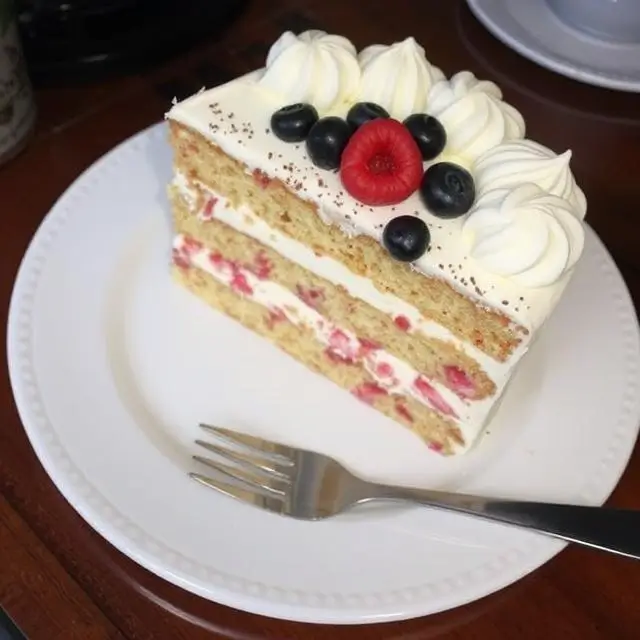 Layer Cake génoise décorée de fruits frais et de fleurs comestibles sous une lumière tamisée.
