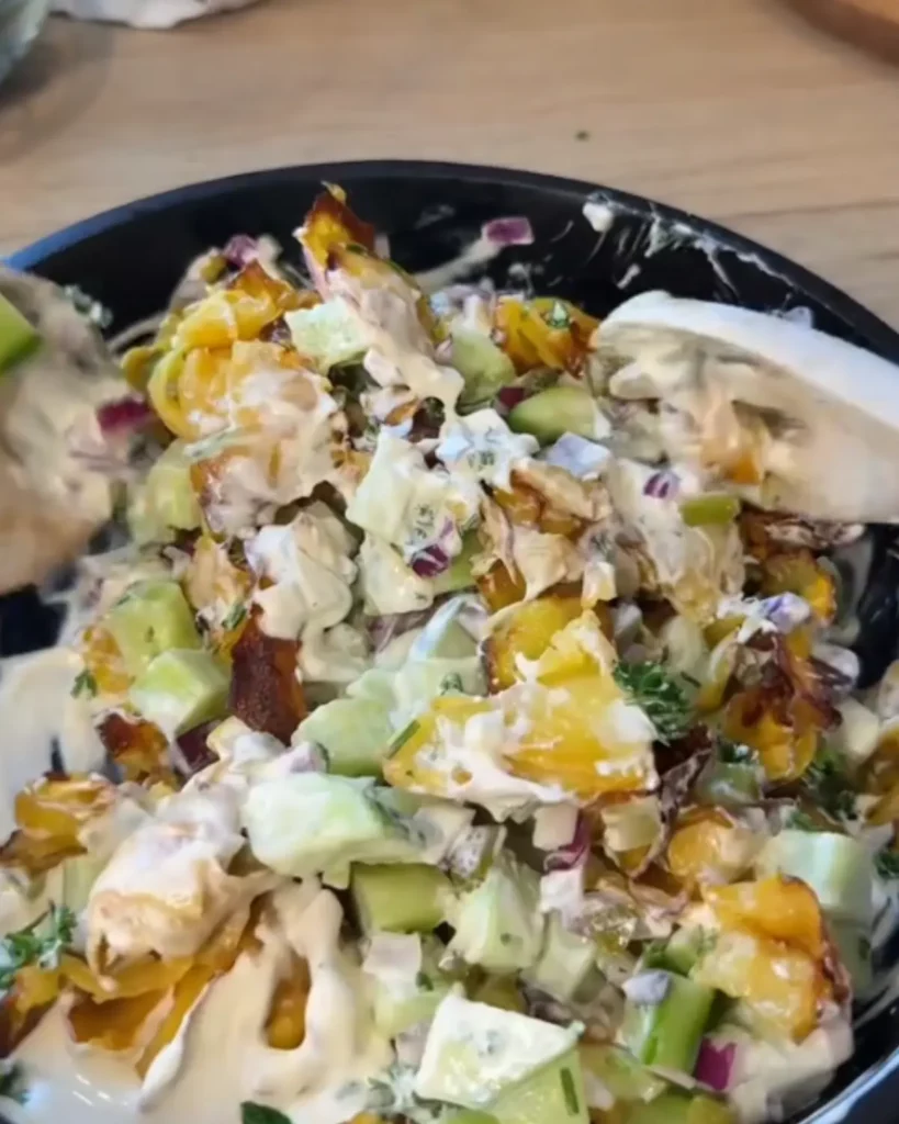 Salade de frites croustillantes enrobées de sauce yaourt grec, cornichons, oignon rouge et herbes fraîches